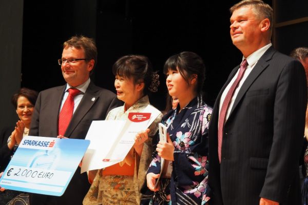 Bürgermeister Hannes Heide bei der Überreichung des Siegerschecks an die Chorleiterin des Seisen Highschool Choir, Mikiko Sato, Japan