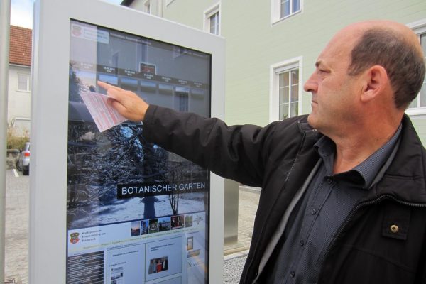 Bürgermeister Hans Baumann führt die vielen Funktionen des interaktiven Informationsbildschirms vor dem Gemeindeamt vor.