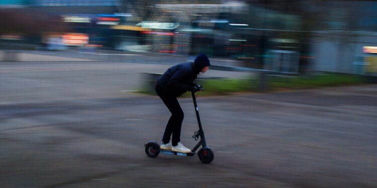man in black jacket riding black kick scooter on road during daytime